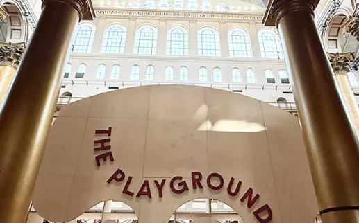 Wooden sign for The Playground inside the Great Hall of the National Building Museum under arched windows
