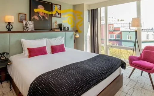 Photo of bright bedroom with king bed, pink pillows and chair, balcony view through large windows