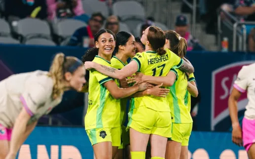 Soccer players in neon yellow hug in celebration while opponents in pink shorts stand nearby
