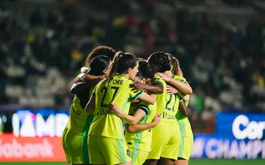 Group of soccer players in neon green jerseys huddle on the field in a stadium