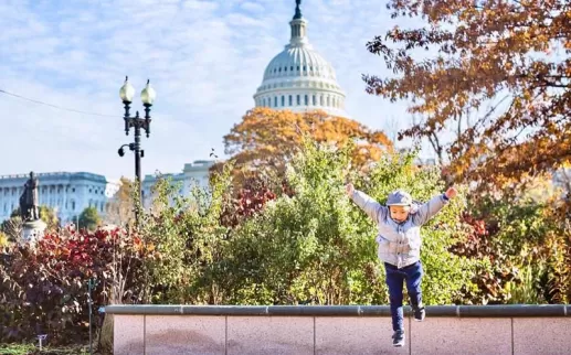 @chasingkaiphoto - Child jumping in front of the U.S. Capitol building surrounded by fall foliage - Fall in Washington, DC
