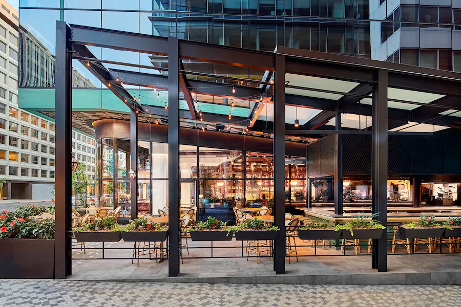 modern outdoor patio dining with plants, covering, and mirrored skyscraper behind