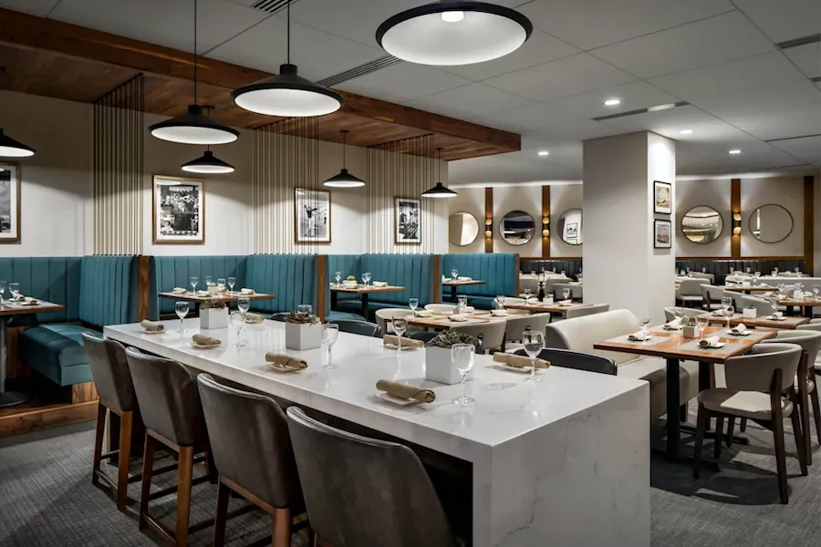 sleek restaurant interior with a white marble countertop in the foreground and other tables and teal blue booth in the background