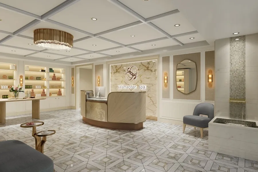 A luxurious spa reception area with elegant, light-colored decor. The reception desk is made of marble, with shelves displaying various beauty products. The room is well-lit with chandeliers and soft lighting.