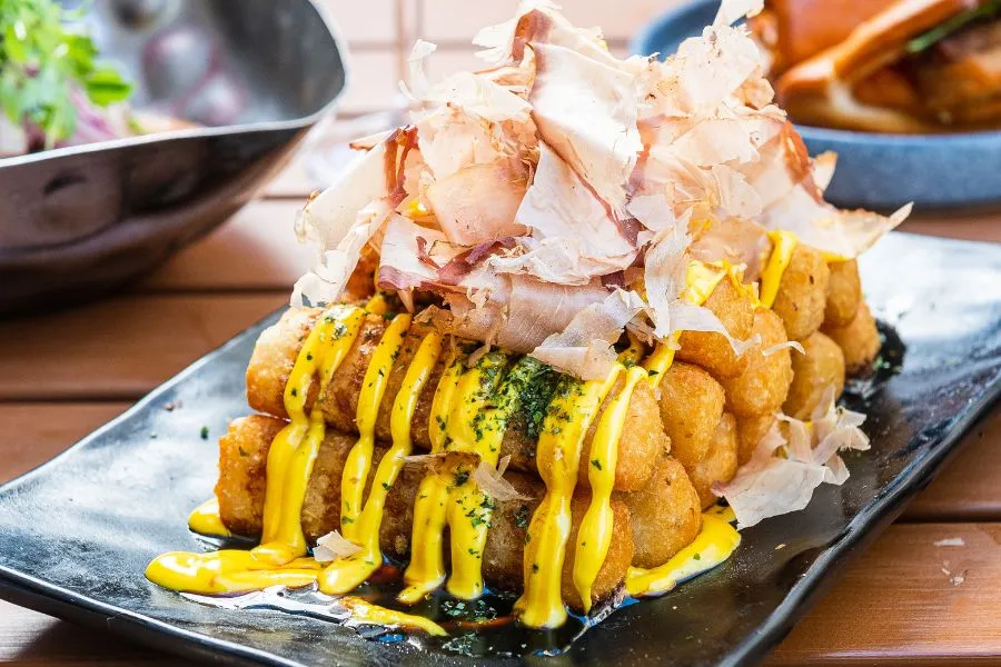 Dancing Yucca at China Chilcano featuring two layers of fried yucca sticks, drizzled with ají amarillo mayo and kabayaki sauce and topped with bonito flakes