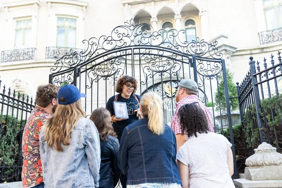 A tour guide speaks to a group outside of an ornate gate to a DC embassy. 