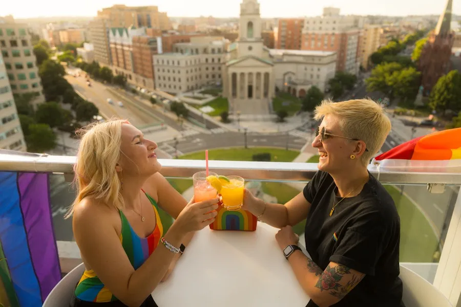 A couple enjoying a cocktail on a rooftop with a view of historic city buildings below. 