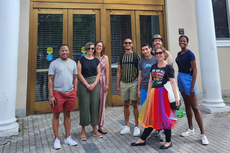 A group smiles for a photo outside a historic theater in Washington, DC with a guide in a rainbow skirt. 