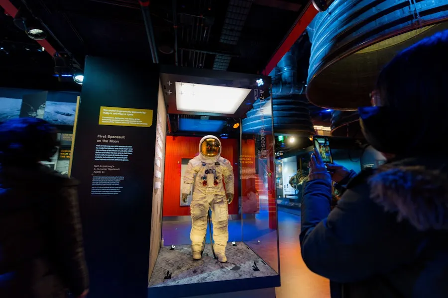 A visitor takes a photo of Neil Armstrong’s Apollo 11 spacesuit on display behind glass.