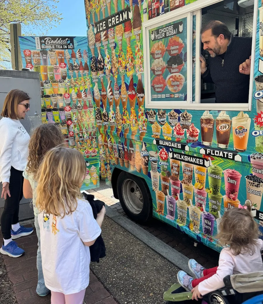 A family looks at the menu of a food truck while the friendly staff member waits for their order. 