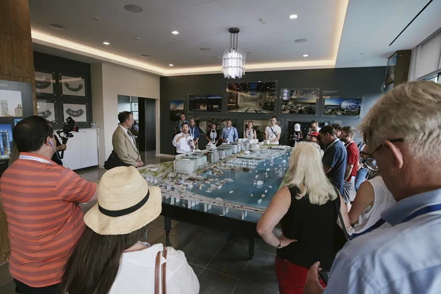 A group of people gathers around a large architectural model of a waterfront development while a guide explains the design.