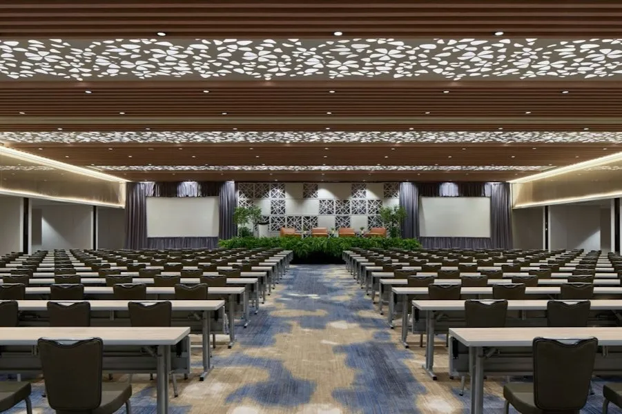 Una grande e moderna sala da ballo allestita per conferenze, con file di tavoli e sedie di fronte a un palco e schermi di proiezione.