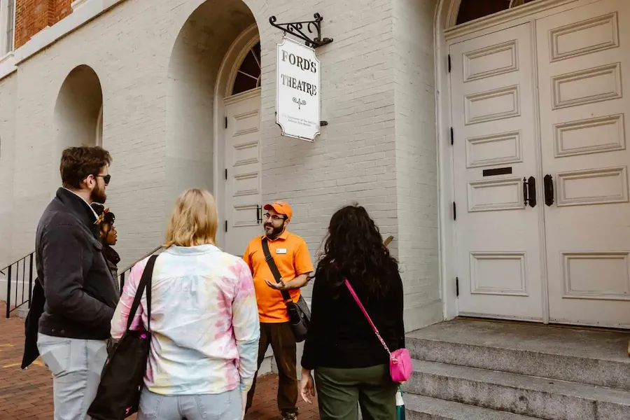 A tour guide in an orange shirt speaks to a small group outside Ford’s Theatre in Washington, DC.