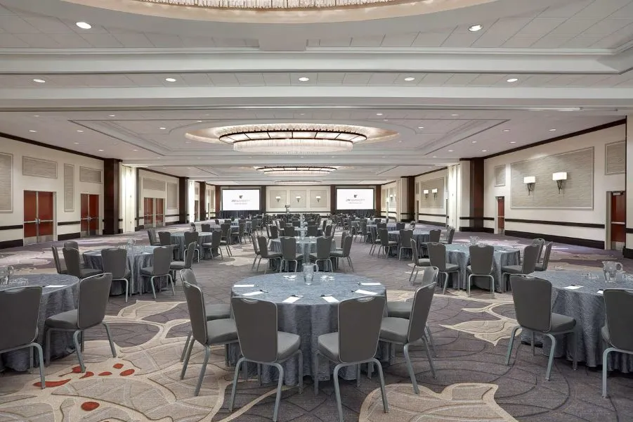 Un'elegante sala da ballo allestita per una cena formale, con lampadari, proiezioni luminose a forma di stella, tavoli rotondi con tovaglie rosa e centrotavola floreali.