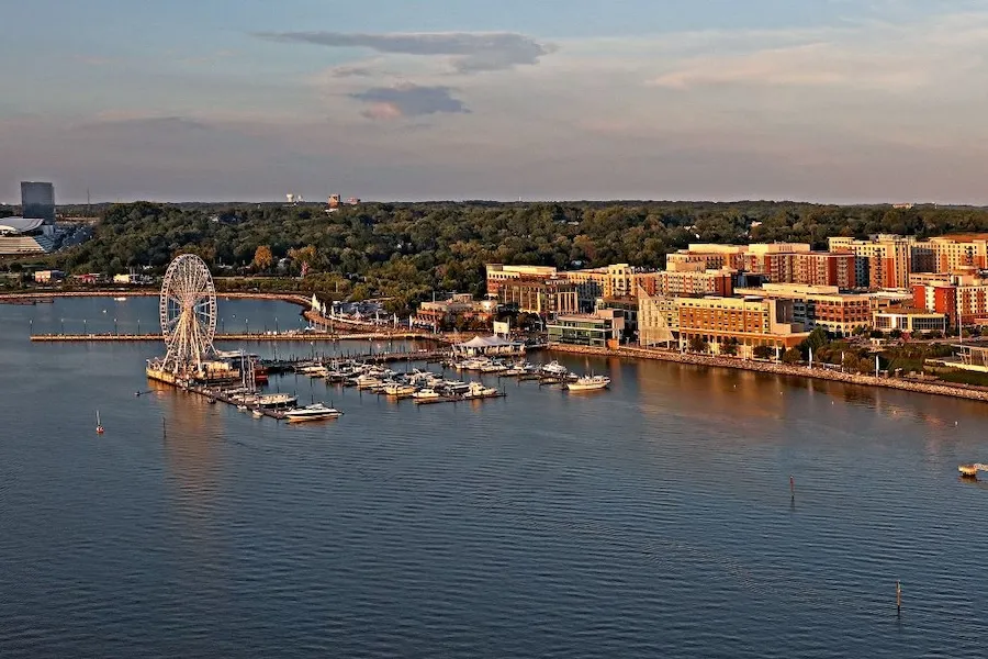 An aerial view of National Harbor at sunset, featuring the Capital Wheel, marina and waterfront hotels along the Potomac River.