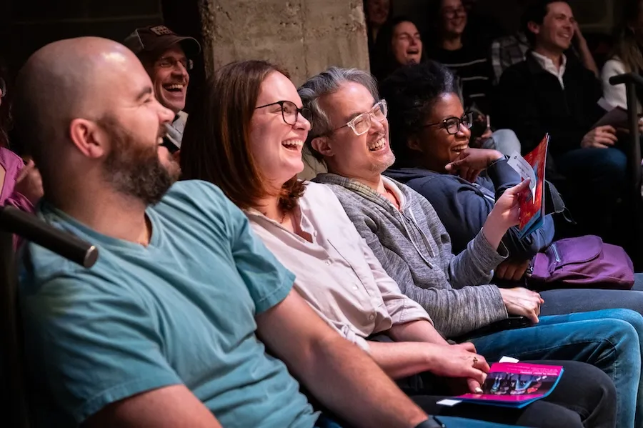 A group of people in the audience laughing and enjoying a live comedy or theater performance.