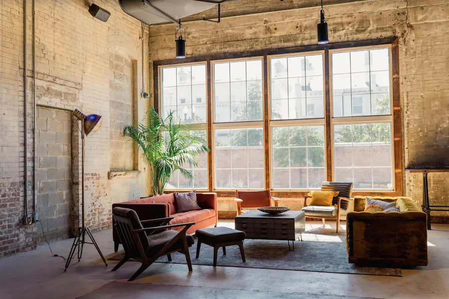 Cozy industrial-style lounge with large windows, vintage furniture, and natural light streaming in.
