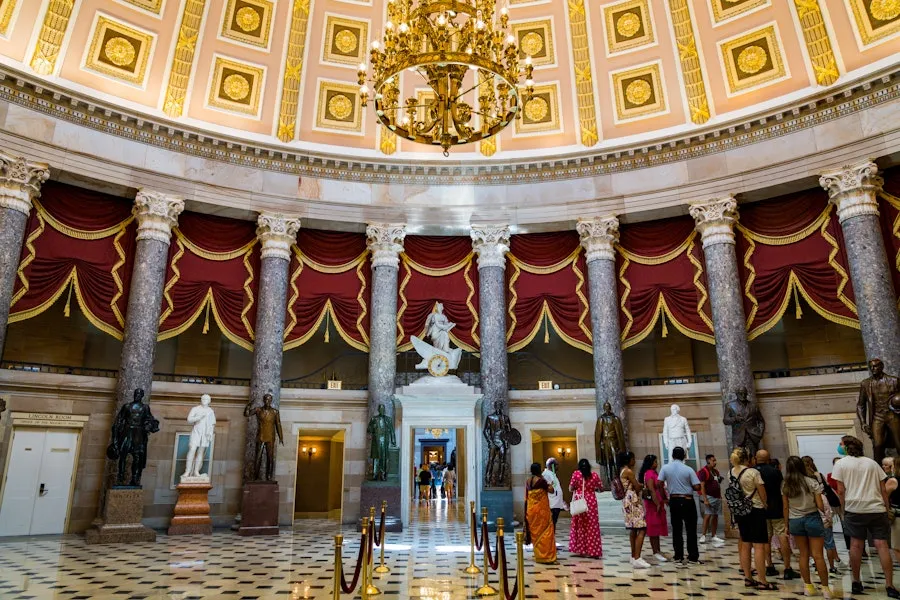 Visitors stand beneath the ornate dome and red curtains of the National Statuary Hall inside the U.S. Capitol.