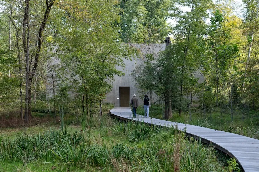 Visitors walk along a curved boardwalk toward the concrete building that houses Richard Serra’s “Four Rounds: Equal Weight, Unequal Measure.”