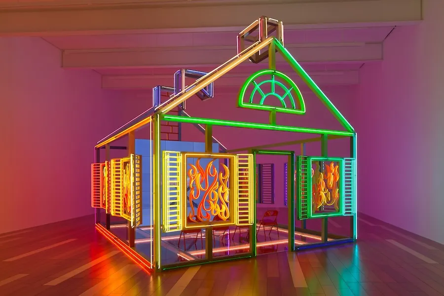 Alex Da Corte’s neon sculpture “Rubber Pencil Devil (Hell House)” glows in vibrant colors, shaped like a house with flames in the windows.