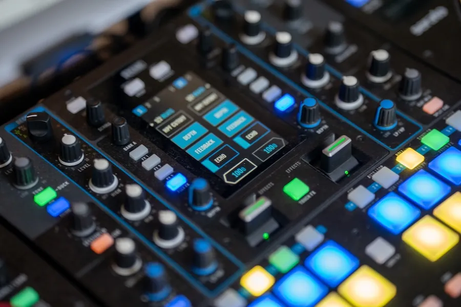 A close-up view of a colorful DJ mixing board shows illuminated buttons, knobs, and sliders during an audio setup.