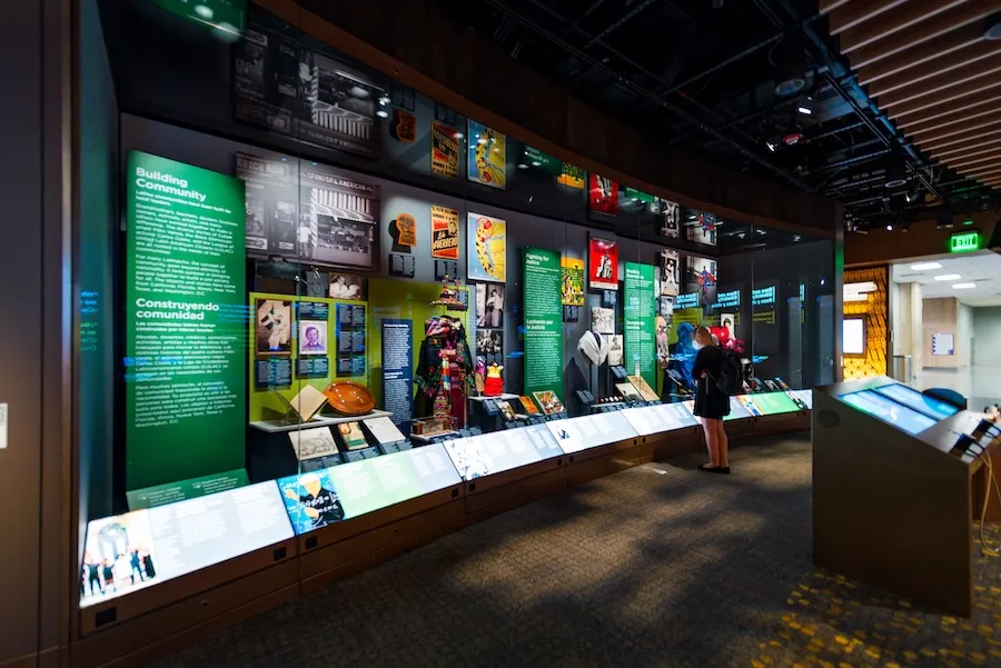 Visitors explore an interactive exhibition gallery at the National Museum of American History in Washington, DC, featuring illuminated displays, artifacts, and interpretive panels.