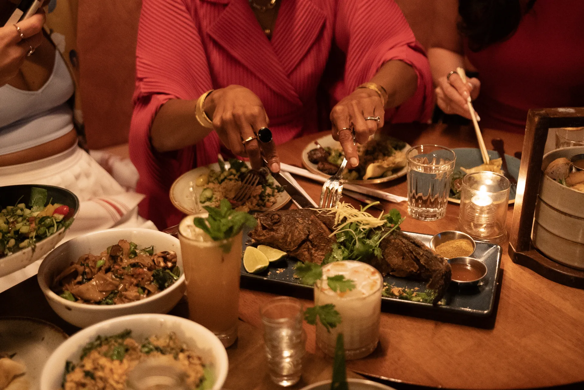 Hands reach across a table to share family-style Vietnamese dishes and cocktails at Doi Moi in Washington, DC, with small plates, herbs, and candlelight creating a warm dining scene.