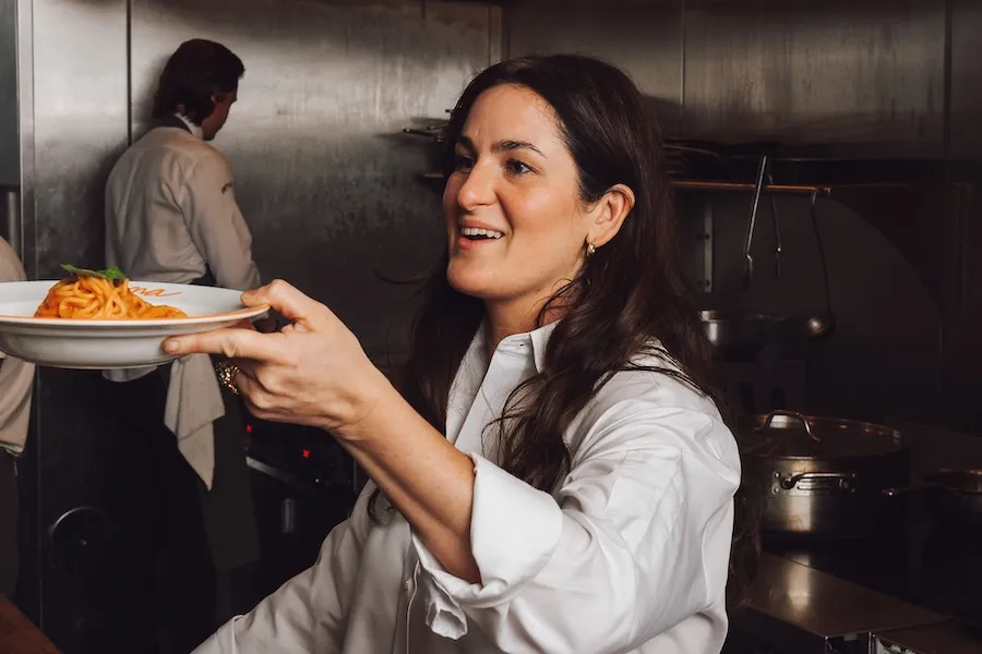 A smiling chef holds out a plate of pasta.