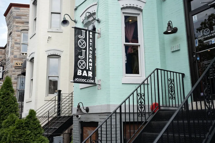 Pastel rowhouse exterior with stairs leading up to the JoJo Bar restaurant entrance.
