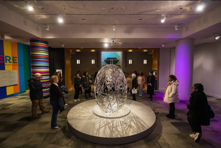 People viewing a large sphere sculpture in a gallery with colorful wall panels