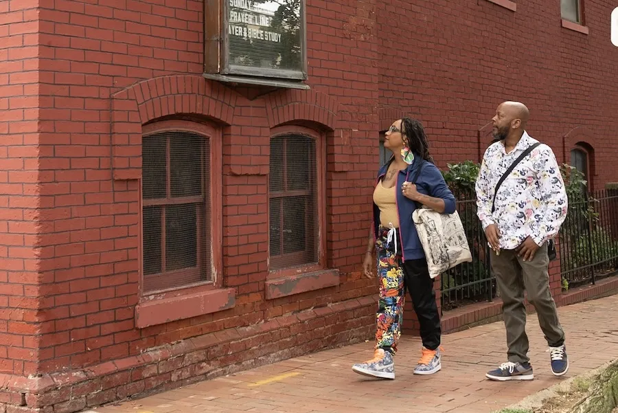 Two people walking along a red brick building on a sunny day