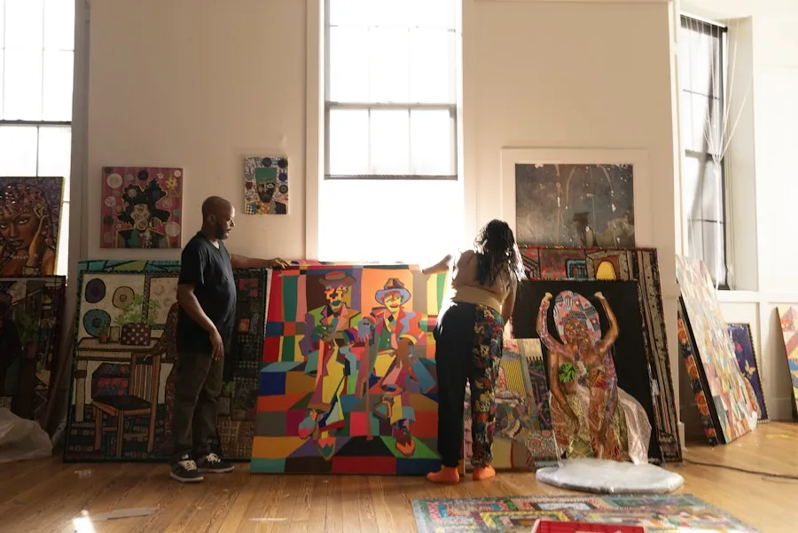 Two people in an art studio with colorful paintings leaning against sunlit walls