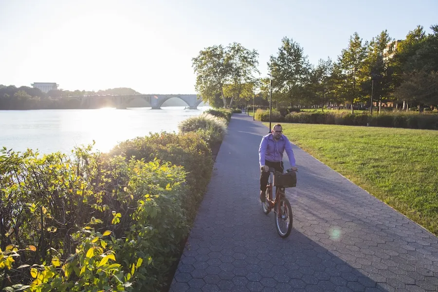 Cyclist on a riverside path at sunset, with trees and green grass nearby