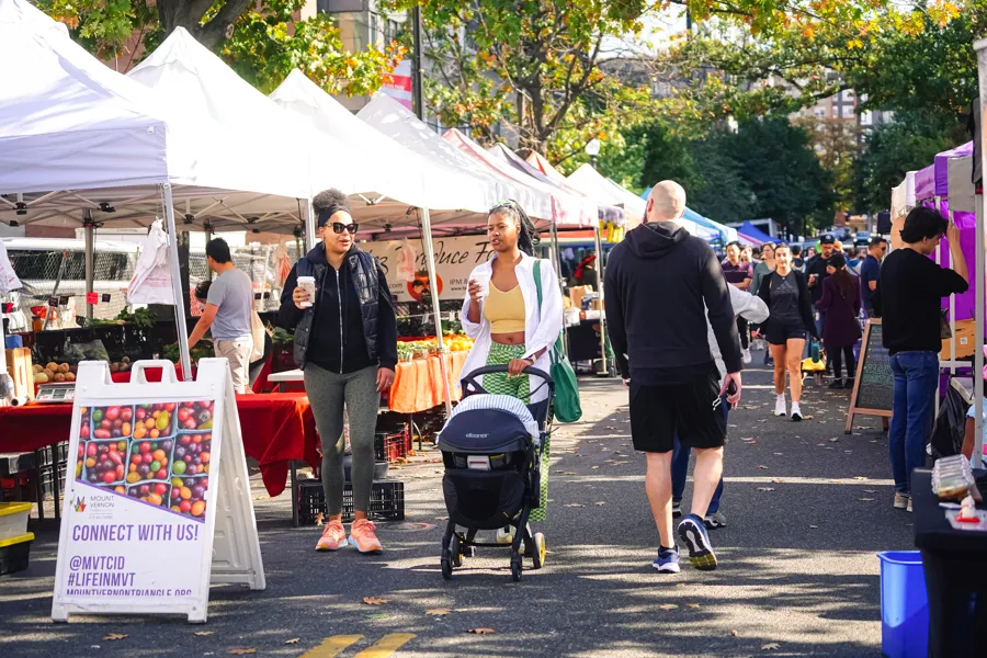 Busy outdoor market on a tree-lined street with vendor tents and pedestrians