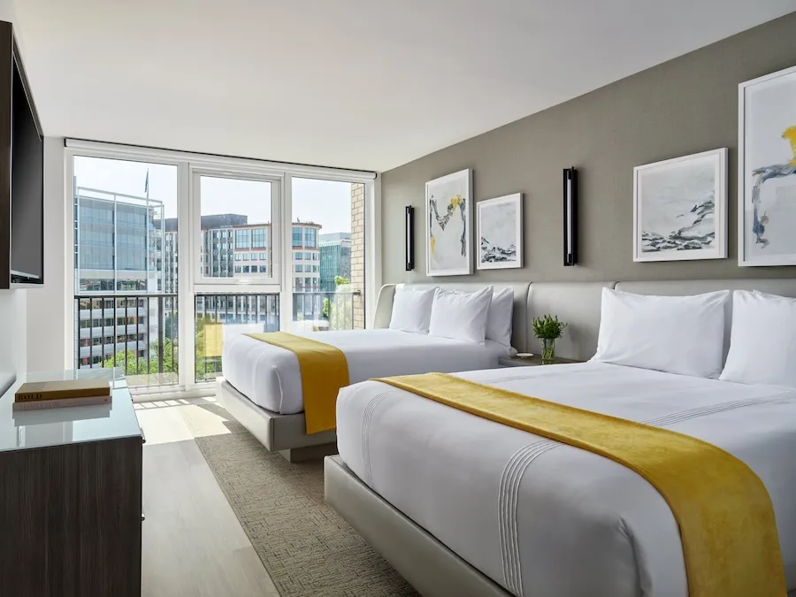 Modern hotel room with two beds and city view through large windows