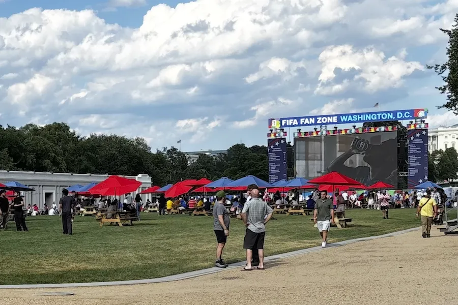 Outdoor festival with red umbrellas, picnic tables and large screen