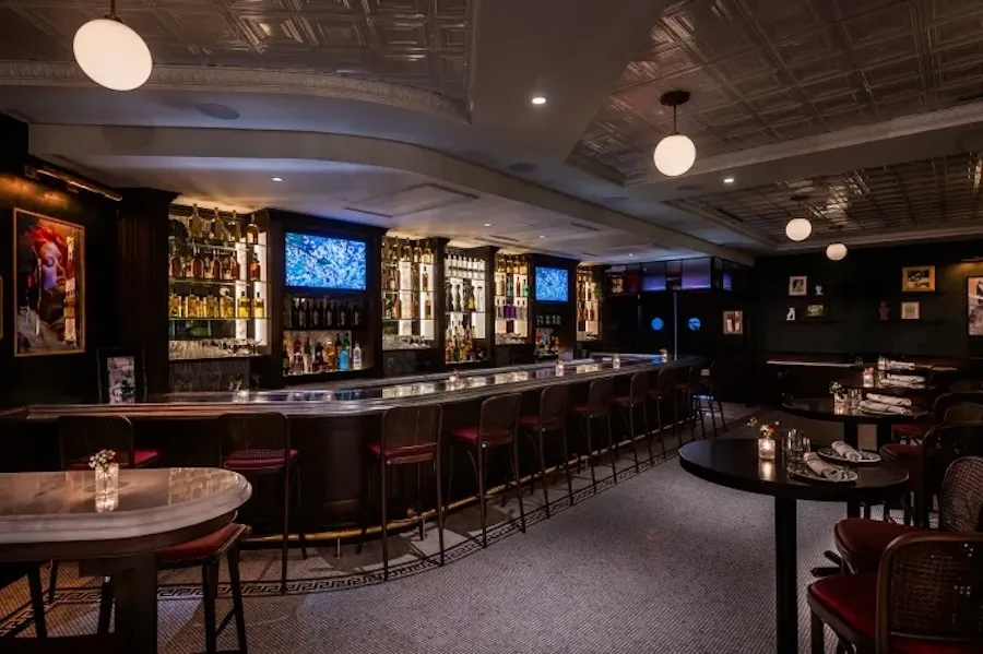 Dimly lit bar with high-top tables and long row of stools