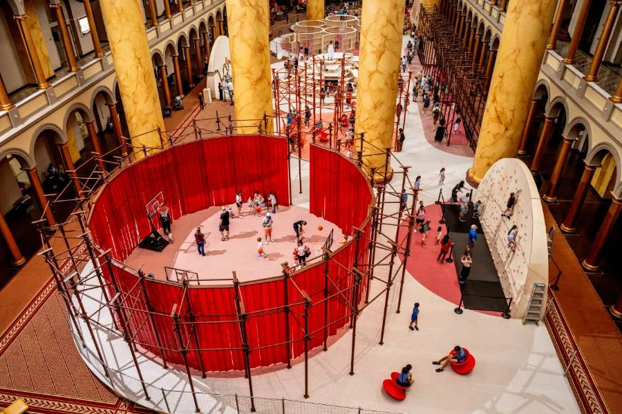 Wide view of the National Building Museum’s Great Hall transformed by the interactive PLAYGROUND exhibition, featuring climbing structures, play areas and hands-on installations.