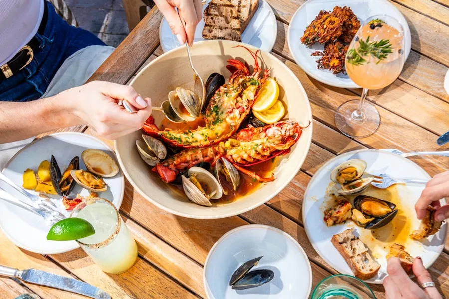 Friends sharing seafood and wine around a wooden table outdoors