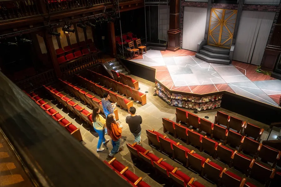 Empty Folger Shakespeare Library Theater with red seats and people walking down an aisle toward the stage
