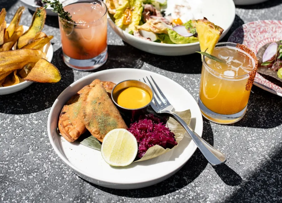 Plates of empanadas and salad with citrus drinks on a sunny patio table