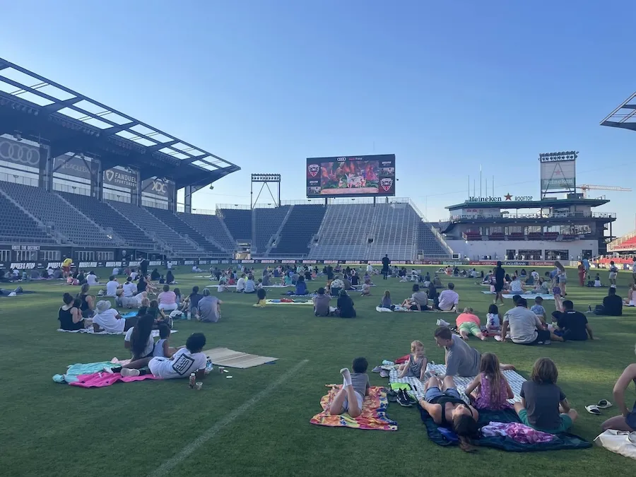 People lounging on a stadium field on blankets in sunny weather