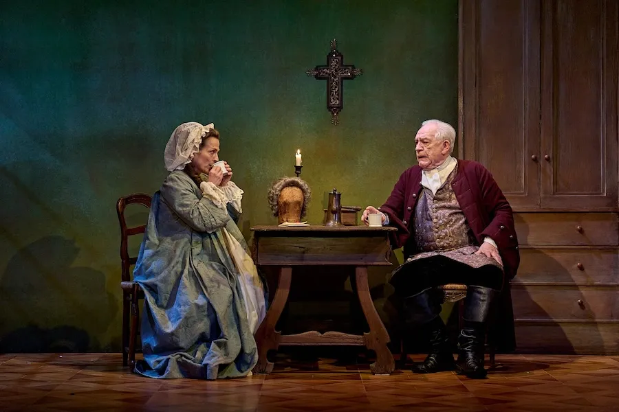 Two people seated at a table on a stage in historical dress
