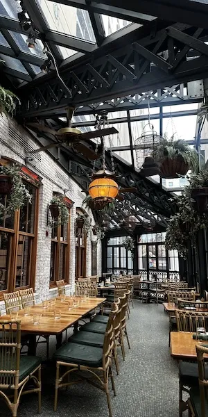 Indoor restaurant patio with wooden tables, green chairs and glass roof with hanging plants