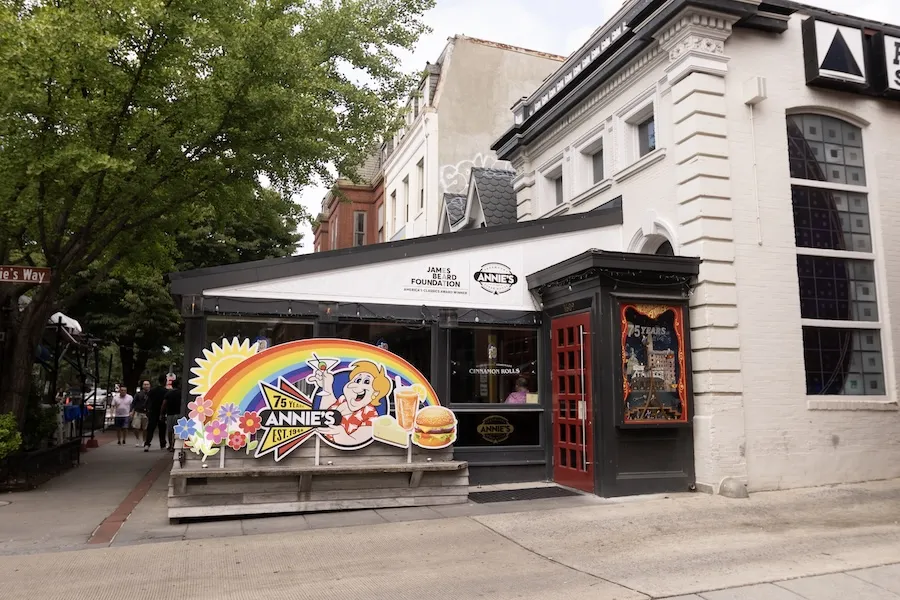 Colorful mural on a white corner building with outdoor patio seating under awnings