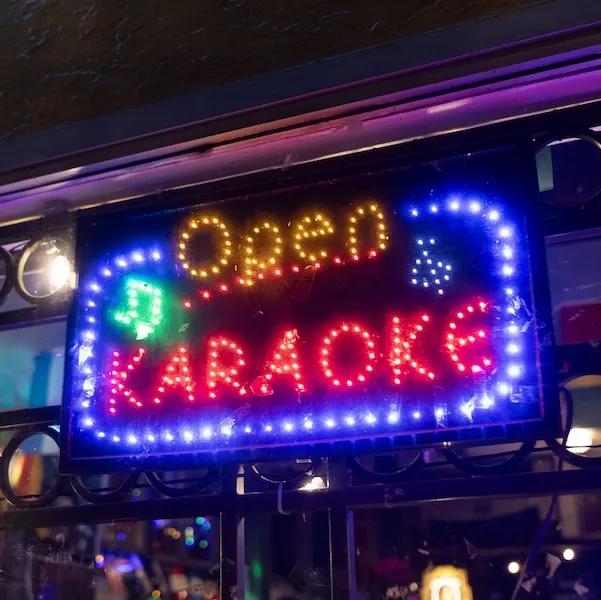 Neon sign reading “Open Karaoke” in blue, red and yellow lights at night