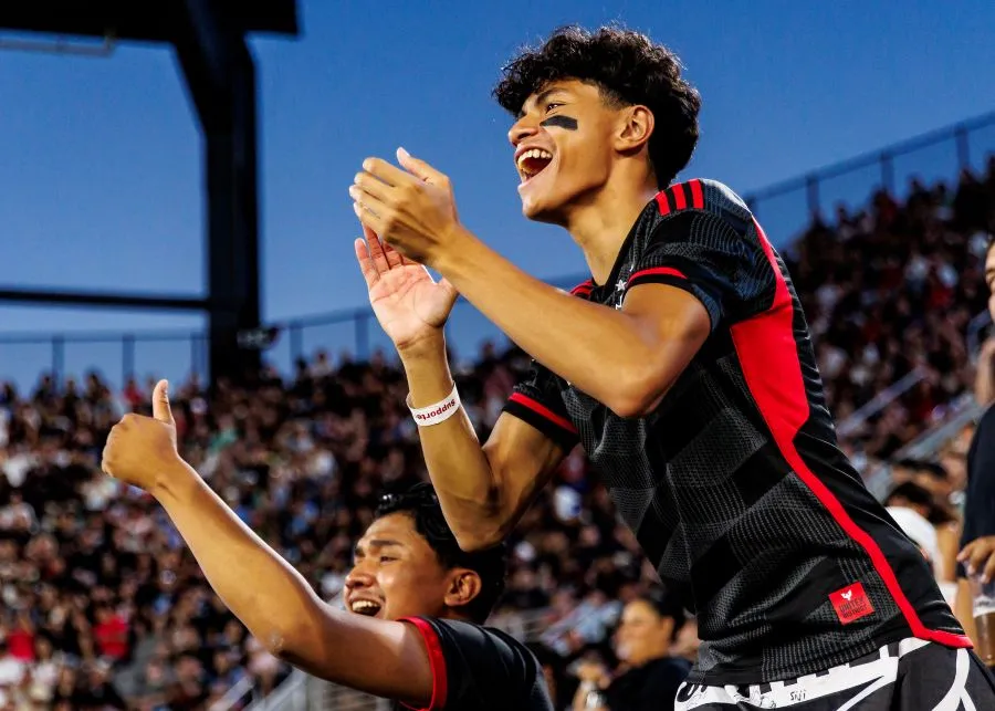 D.C. United fan in black and red uniform claps as crowd cheers in stadium