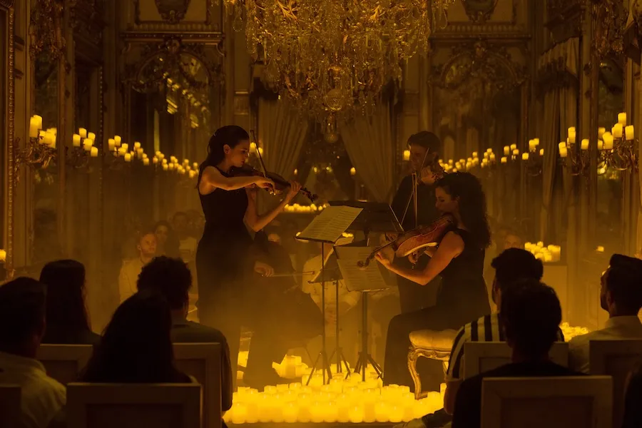 Candlelit chamber concert with string players onstage and seated audience in a golden hall