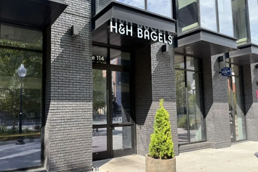 Photo of H&H Bagels storefront with glass windows and a potted evergreen tree