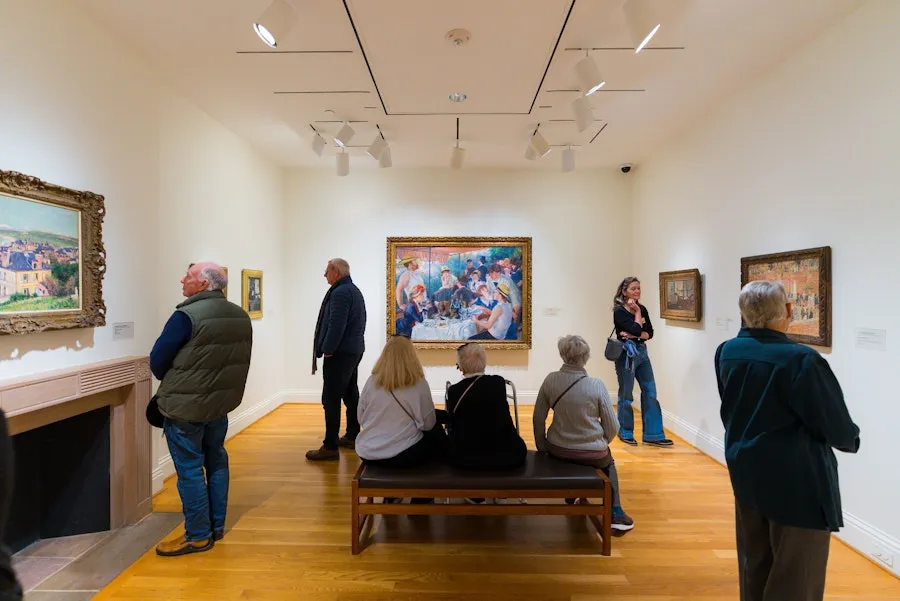 Visitors sit and stand in a bright gallery in The Phillips Collection viewing paintings.